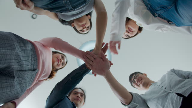 Bottom up view : Group of happy asian employee joining stack hands together, smiling in brainstorm meeting at office. Casual business with startup teamwork community celebration concept.