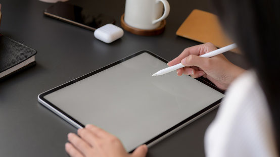 Cropped shot of a woman drawing on mock up tablet with stylus and other wireless device on black table background