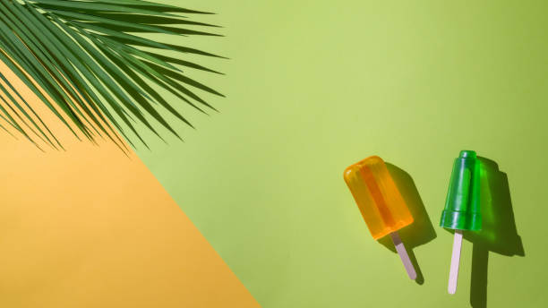 Top view of lime and orange flavour popsicles, palm leaf and copy space on flat lay yellow and  green background
