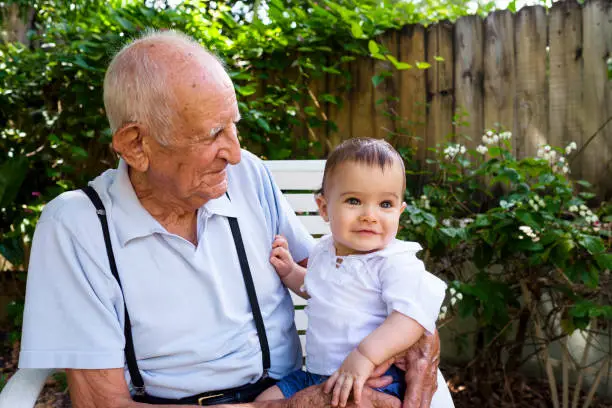 Cute baby boy with great grandfather in a backyard home garden setting.
