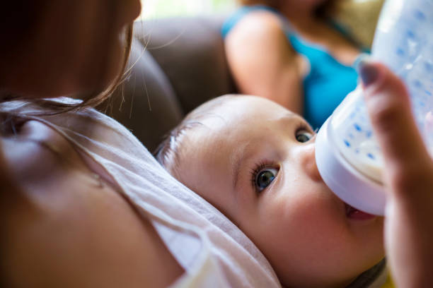 Baby boy and young mother Pretty young woman feeding a cute baby boy indoors in a home setting. baby bottle stock pictures, royalty-free photos & images