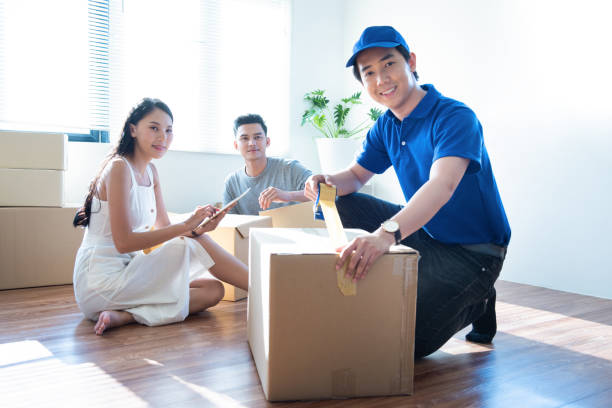 istock Delivery service worker man in blue uniform help happy couple customer packing parcel with tape in customer home. 1206763357