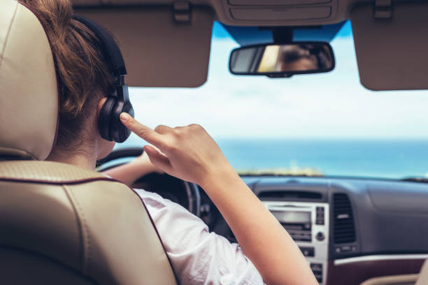 mujer conductora en los auriculares conduciendo un coche. chica relajándose en viaje en auto viajando a lo largo de la playa tropical del océano en el fondo. concepto de viajero. vista posterior - tropical climate audio fotografías e imágenes de stock