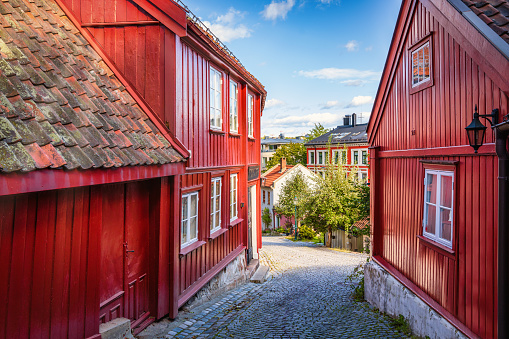 Red woodenhouses in old town village in Damstredet Cobblestone Street in Oslo under blue summer sky. One of the oldest streets in the historic center of Oslo, Capital of Norway. Damstredet, Oslo, Norway, Scandinavia