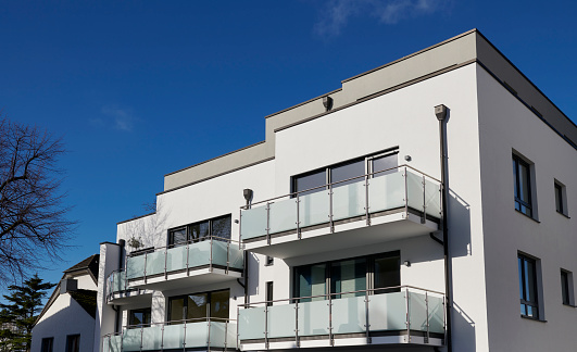 Part of modern white apartment houses with balconies and deep blue sky.