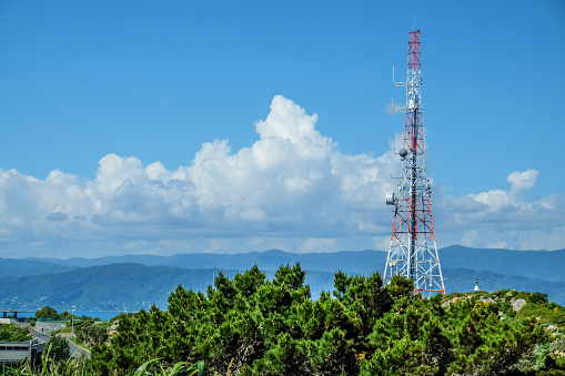 Close up shot of telecommunication tower antenna on top of a mountain, with a blue sky background, during summer in a lush green park