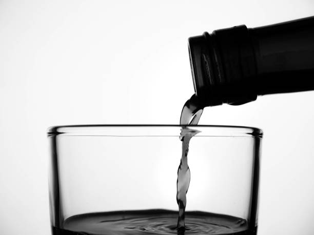 Close up of pouring fruit juice from green bottle into glass, isolated on white background.