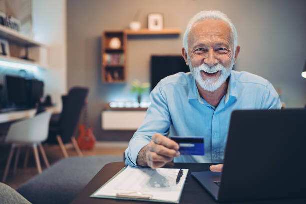 hombre mayor compra ndo en línea usando una tarjeta de crédito - surfista de plata fotografías e imágenes de stock