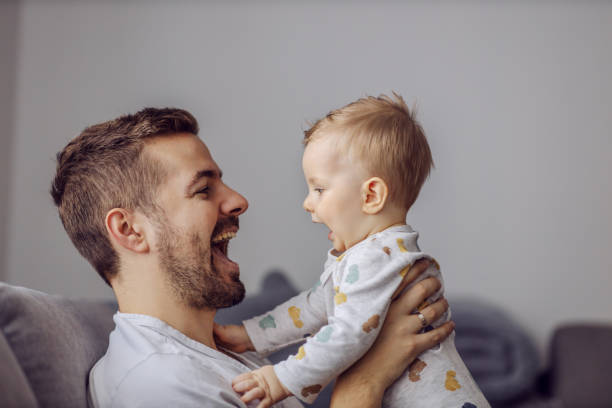 Adorable little blond boy playing with his caring father and biting his nose. Father is smiling. Caring father holding his only beloved adorable little boy and teaching him to talk. dad and baby stock pictures, royalty-free photos & images