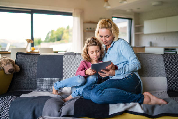istock A cute small girl with mother on sofa indoors at home, using tablet. 1206803727