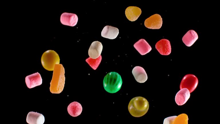 SLO MO LD Colourful candy falling down against black background