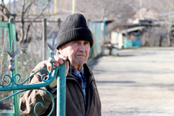 Elderly man opens the iron gate in rural yard Unhappy face expression, concept of cold weather, life in village, old age russian ethnicity stock pictures, royalty-free photos & images