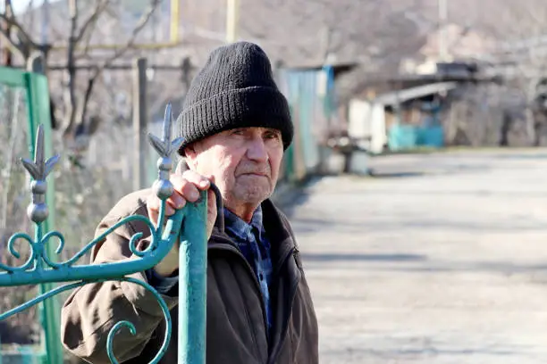 Photo of Elderly man opens the iron gate in rural yard