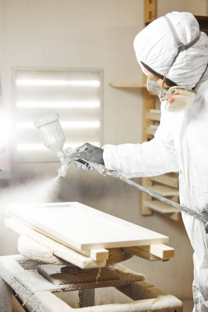istock Man in respiratory mask sprays a gun white paint on wood. 1206804792