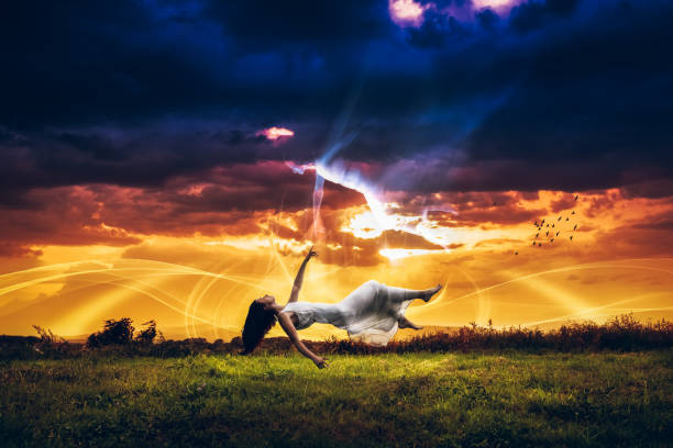Young Caucasian woman levitating in nature in front of light painting trying to reach her reflection above her. Young woman levitating and trying to reach her spirit.