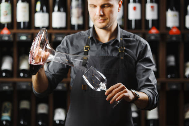 istock Bartender pours red wine in glass from big transparent vessel 1206805383