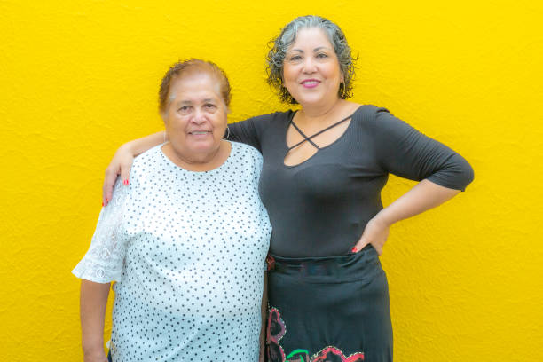 Daughter hugging her mother very smiling, two Mexican women wearing casual clothes on a yellow background stock photo