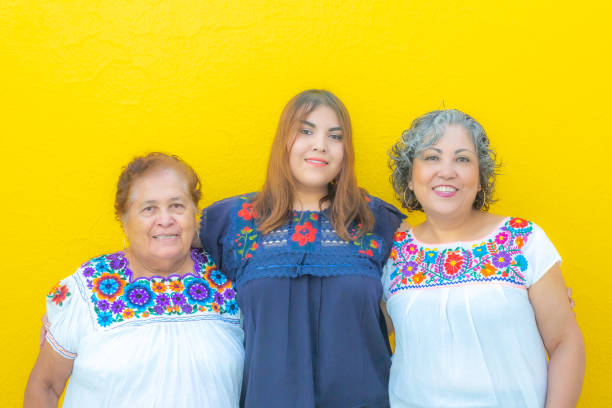Three generations of Mexican women smiling wearing floral print blouses looking at the camera stock photo