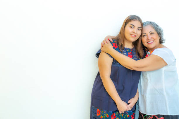 Mother hugging her daughter with a lot of love Mother hugging her daughter with a lot of love, two smiling Mexican women on a white background, space for text hispanic grandmother stock pictures, royalty-free photos & images