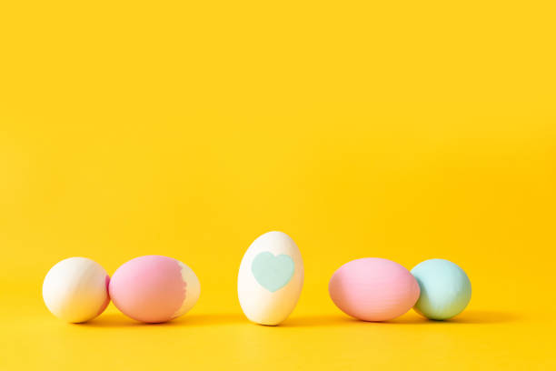 Colorful dyed easter eggs in heart shaped bowl on orange colored background
