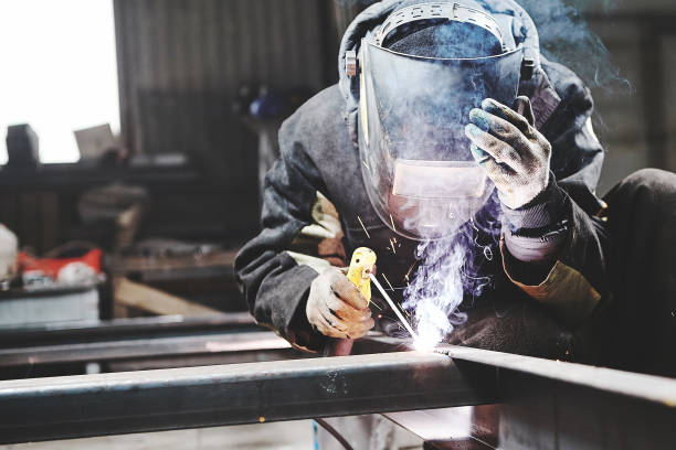 Male in face mask welds with welding Male in face mask, protective gloves welds with welding. Welder makes weld seam on metal frame. Worker dressed in protective clothes. welding mask stock pictures, royalty-free photos & images