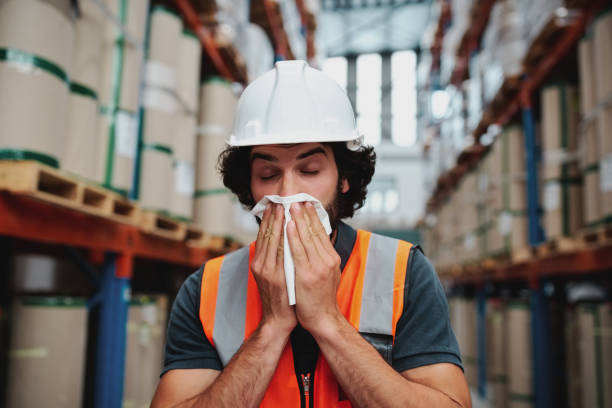 istock Young warehouse manager coughing and sneezing while feeling sick and covering mouth with handkerchief standing in factory 1206809555