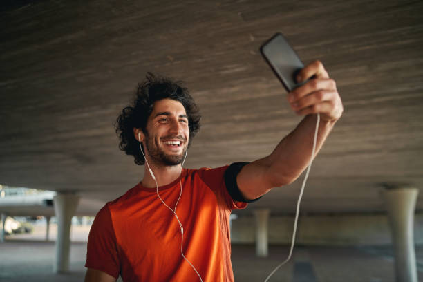 istock Cheerful young man standing under the bridge making video call on his smartphone with earphone - young fit male taking a selfie while exercising 1206810012