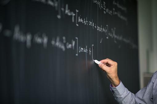 Math teacher by the blackboard during mathclass - detail of the hand with chalk