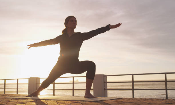 Exercise the body while exercising the mind Shot of a woman practising yoga on the promenade warrior 2 stock pictures, royalty-free photos & images