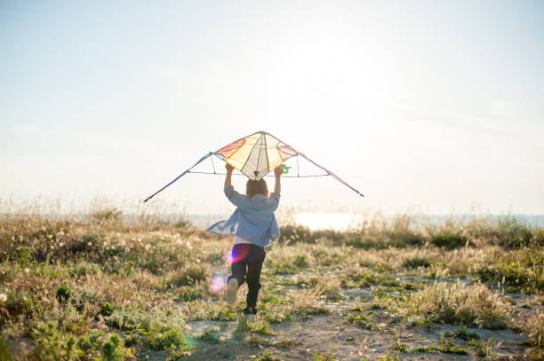 active small boy with kite running to sea on sunset