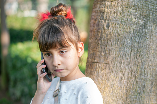 Little girl using her mobile phone by garden