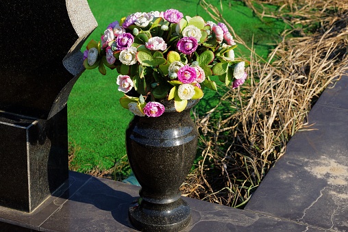 one black marble vase with a bouquet of colored artificial flowers stands on a stone slab in a cemetery