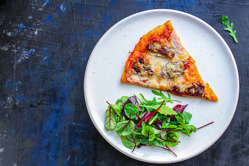 slice of pizza and salad leaves in a plate on the table (tasty snack) menu concept
