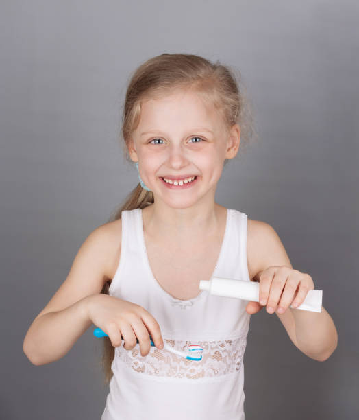 istock Smiling little girl brushes her teeth on a gray background 1206825478