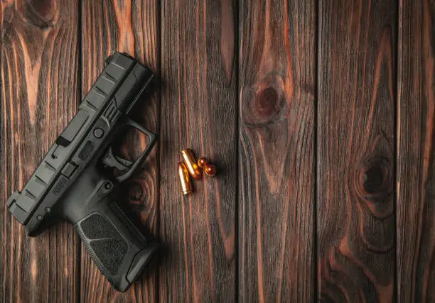 Photo of Modern black gun and ammunition  on a wooden background. Pistol. Weapons for sport and self-defense lie on the table.