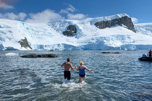 taking a polar plunge in Antarctica Antarctica -  December 17, 2019.  a middle aged couple prepares to take a "polar plunge" into the icy waters on the Antarctic peninsula cold plunge stock pictures, royalty-free photos & images