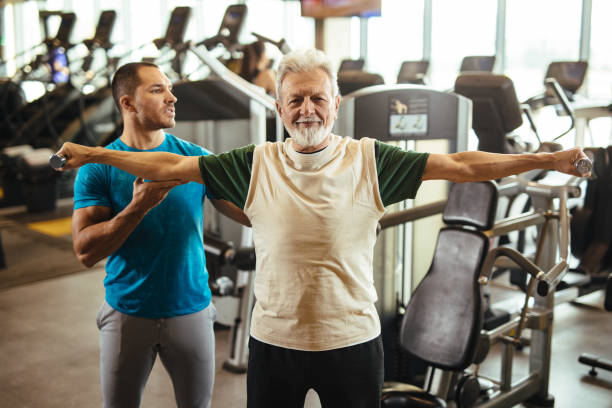 istock Senior man exercising with personal trainer using dumbbells at the gym 1206831634