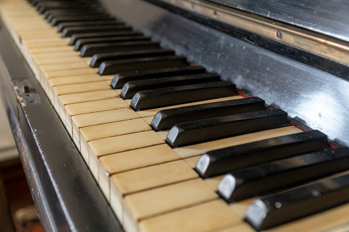 Old piano with damaged keys against wall in an old house.