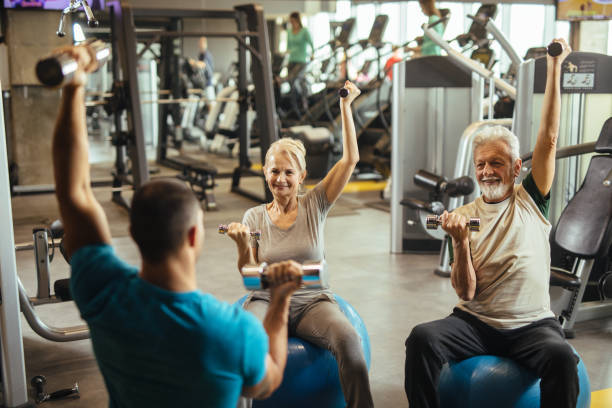 istock Senior couple exercising with personal trainer using dumbbells at the gym 1206833822