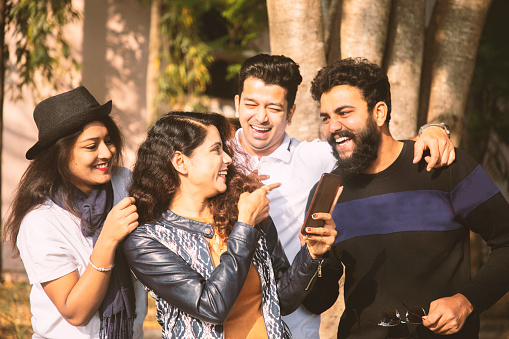 Group of young people laughing by seeing into smartphone - Millennials having fun with friends - trendy modern youth busy on mobile phone, Internet and social media.