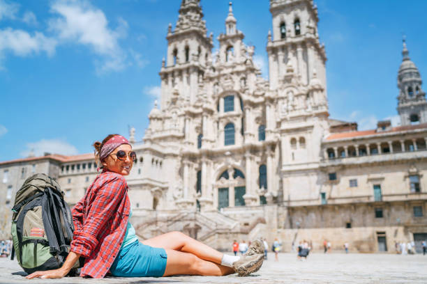 jovem mochileira piligrim sentada na praça obradeiro (praça) em santiago de compostela, espanha. o famoso ponto de chegada de camino de santiago também. - galicia pilgrimage pilgrim religion - fotografias e filmes do acervo