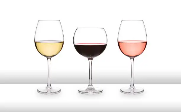 Three glasses of wine, white, red and rose, on a white bar like surface, with a white background