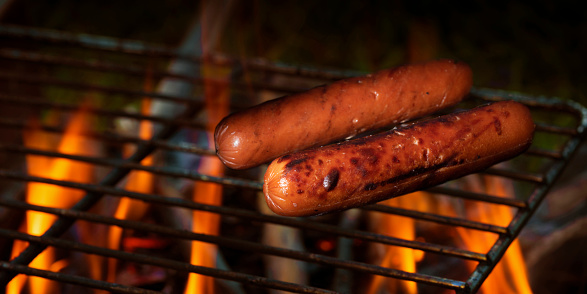 High quality stock photo of an grilled hotdogs cooking over open coasl for a summer time party at home in the backyard.