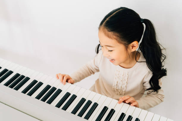 Satisfied Asian kid playing piano at home From above of happy smiling cute Asian girl playing piano enjoying time practicing music at home japan small apartment stock pictures, royalty-free photos & images