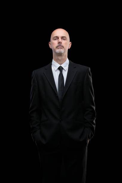 snooty man in black suit on black background arrogant looking man in black suit with tie isolated on black background could be used as doorman bouncer fbi arrogant-business-man stock pictures, royalty-free photos & images