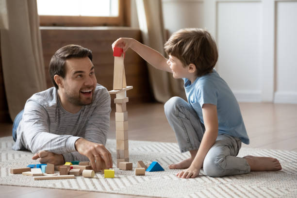 glücklicher vater spielt mit kleinen schuljungen im wohnzimmer. - living room people joy happiness stock-fotos und bilder