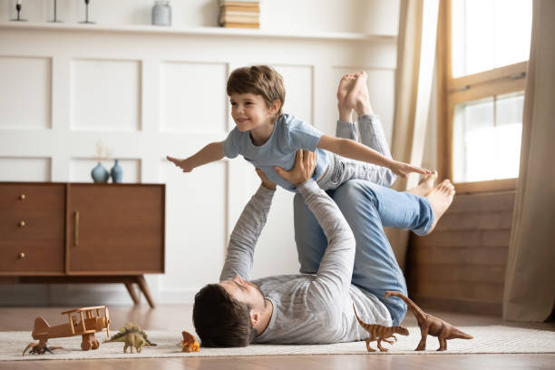 Joyful young man father lifting excited happy little son. Joyful young man father lying on carpet floor, lifting excited happy little child son at home. Full length carefree two generations family having fun, practicing acroyoga in pair in living room. exercising photos stock pictures, royalty-free photos & images