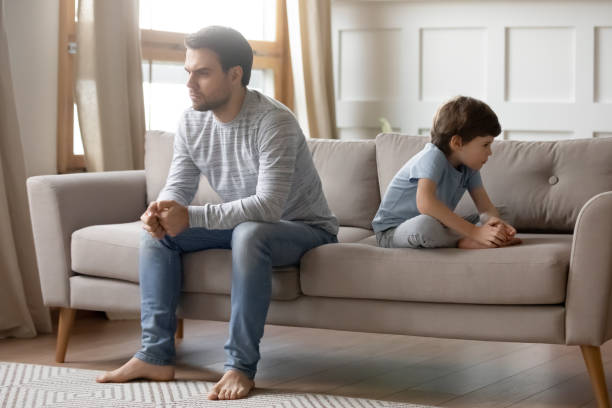 istock Annoyed young father sitting back to back with little son. 1206859205