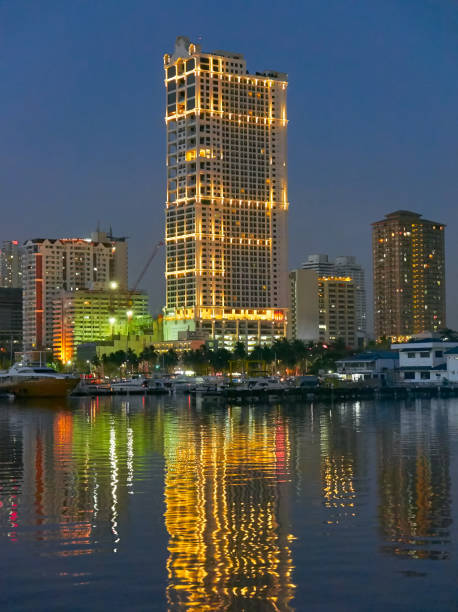 Night scenery of boats docking at Manila Bay near Manila Yacht Club with illuminated skyscraper buildings in the background reflecting in the water