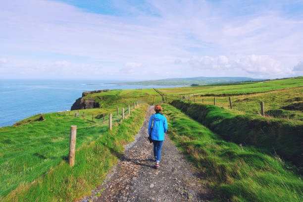 Woman trekking on Cliffs of Moher walking trail in Ireland Woman trekking on Cliffs of Moher walking trail in Ireland county clare stock pictures, royalty-free photos & images